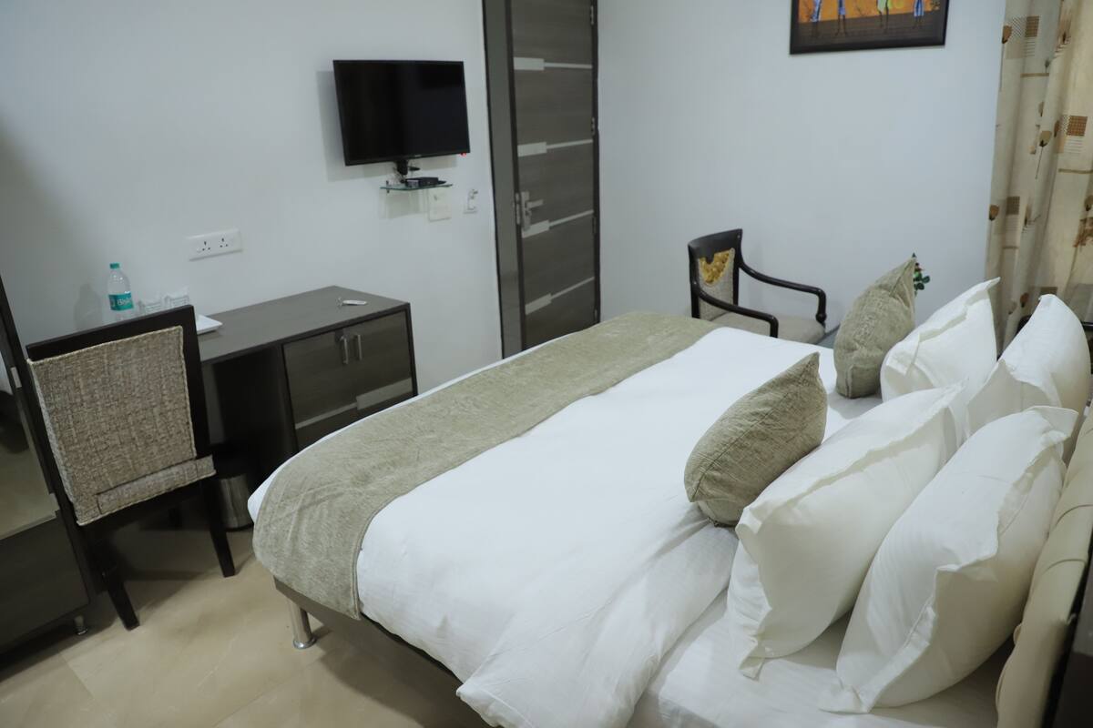 Una habitación de hotel con cama, escritorio, silla, televisor y armario.