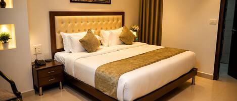 A hotel room with a large bed, a bedside table with a phone, a nightstand, and a painting on the wall.