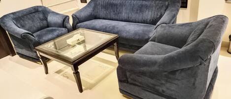 A room with a blue sofa set, a glass coffee table, and a white chair.