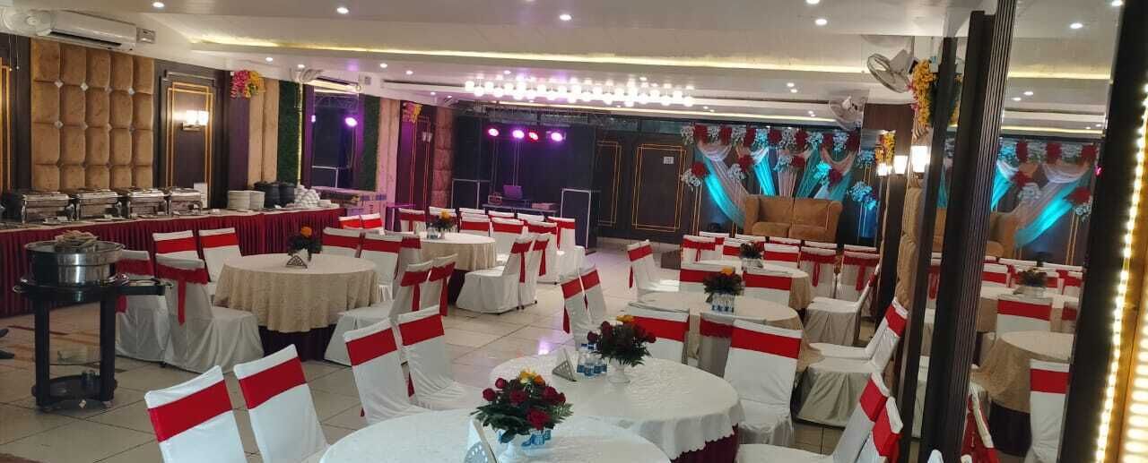 Una sala da banchetti con tavoli rotondi, coperture rosse e bianche per le sedie e un palco illuminato.