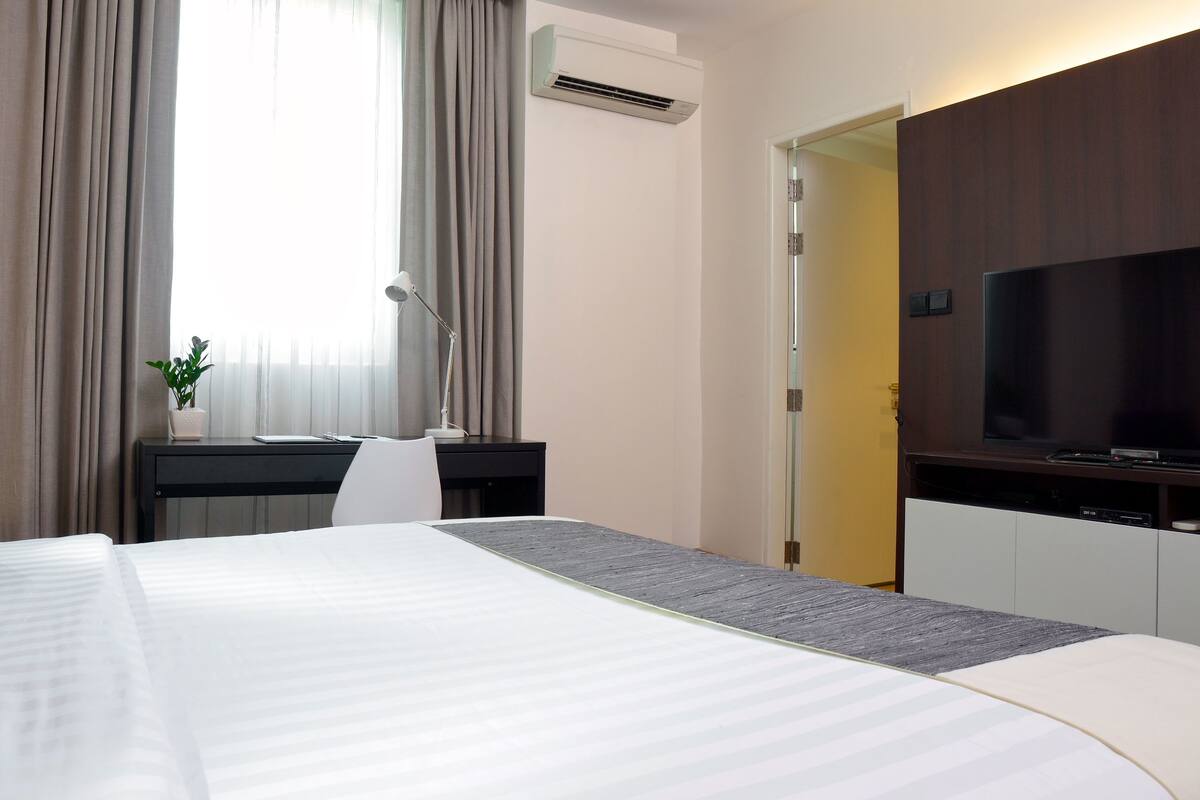 Une chambre d’hôtel avec un grand lit, un bureau avec une lampe, une télévision et un appareil de climatisation.