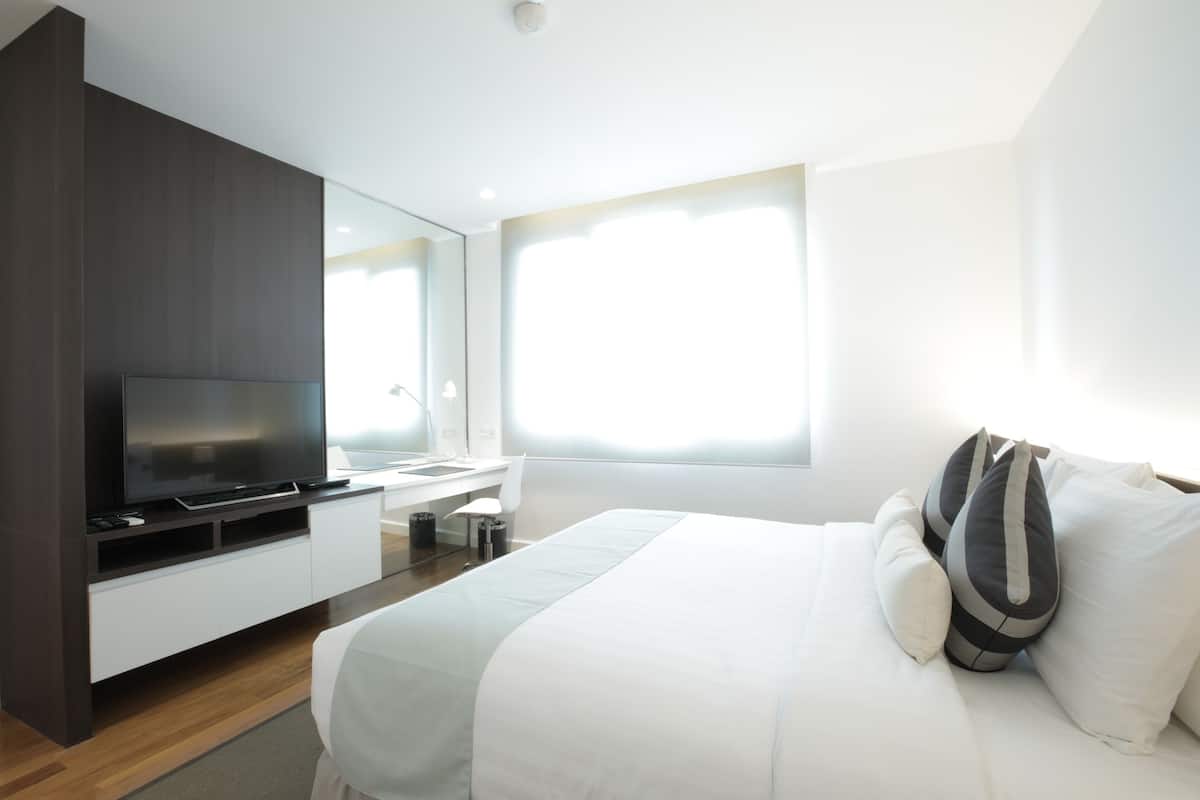 Une chambre d’hôtel moderne dotée d’un grand lit, d’une télévision à écran plat, d’un bureau et d’une grande fenêtre laissant entrer la lumière naturelle.