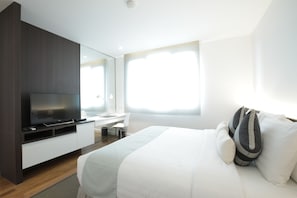 Ein modernes Hotelzimmer mit einem großen Bett, einem Flachbildfernseher, einem Schreibtisch und einem großen Fenster für natürliches Licht.