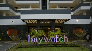 A hotel entrance with a 'baywatch' sign, a modern design, and a landscaped area with palm trees.