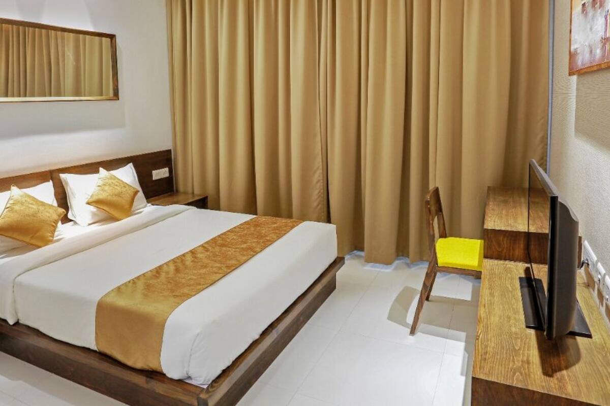 Habitación de hotel con una cama, cabecero de madera, televisor, escritorio y espejo.