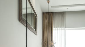 A modern bedroom with a large bed, a hanging orange pendant light, a bedside table with a vase, and a large window with curtains. - Kent Baywatch Suites (Kochi)