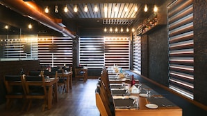 A restaurant with wooden tables and chairs, modern lighting, and large windows with blinds. - Kent Baywatch Suites (Kochi)
