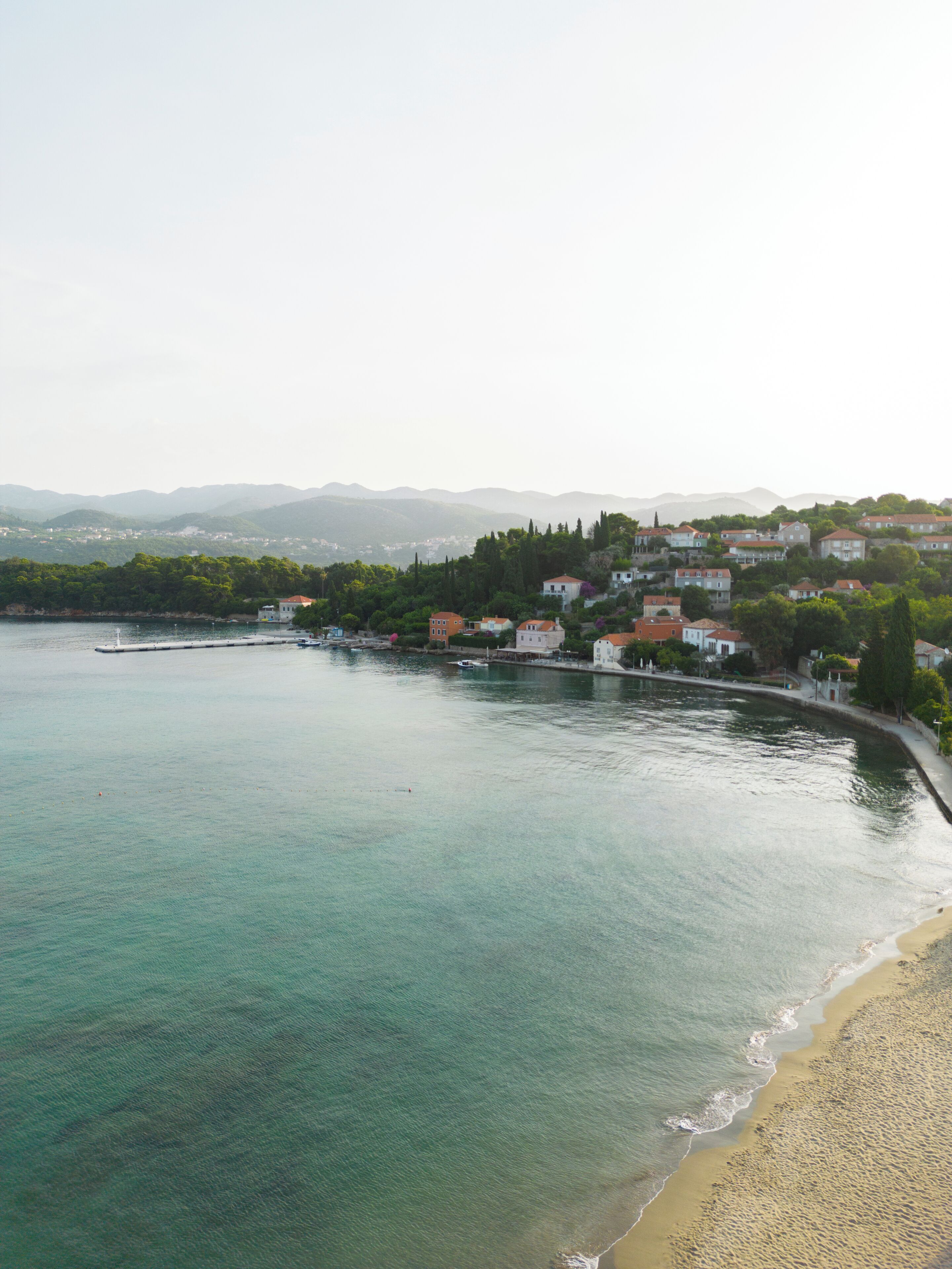 Un poble costaner amb edificis al passeig marítim, una platja de sorra i una vista clara del mar.