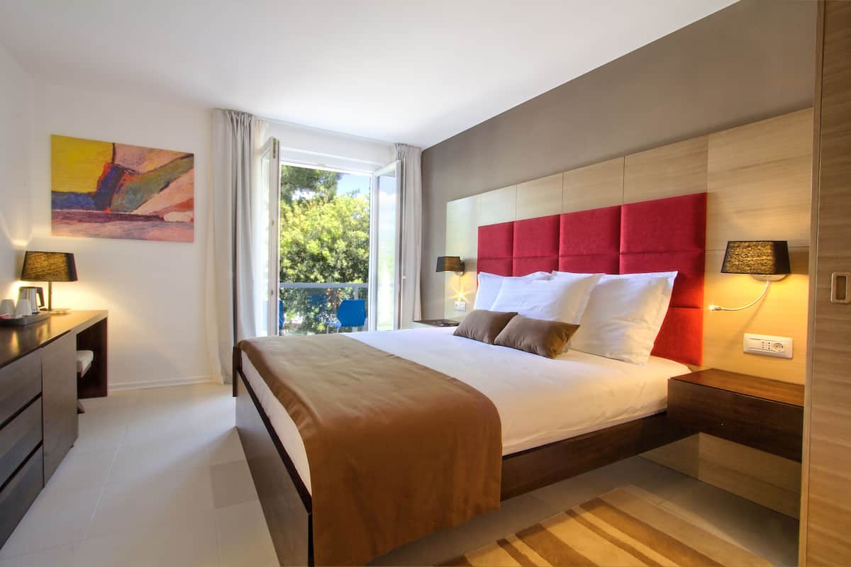 A modern hotel room with a large bed, a desk, and a window with a view of trees.