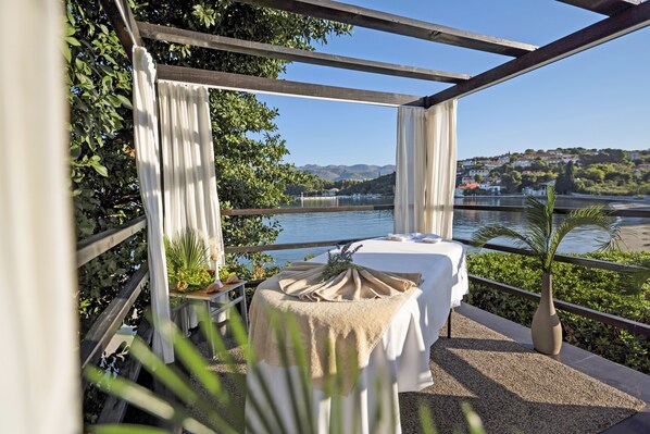 Un balcon avec une table dressée pour deux personnes, offrant une vue sur une rivière et un paysage pittoresque.