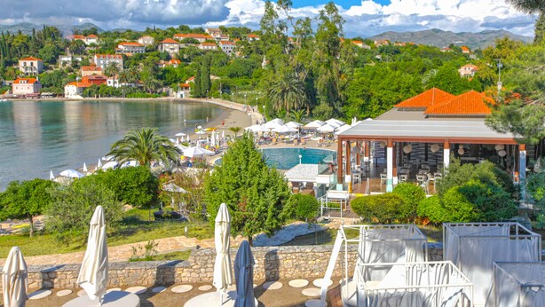 Un resort costero con piscina, mobiliario exterior y vistas al mar y casas cercanas.