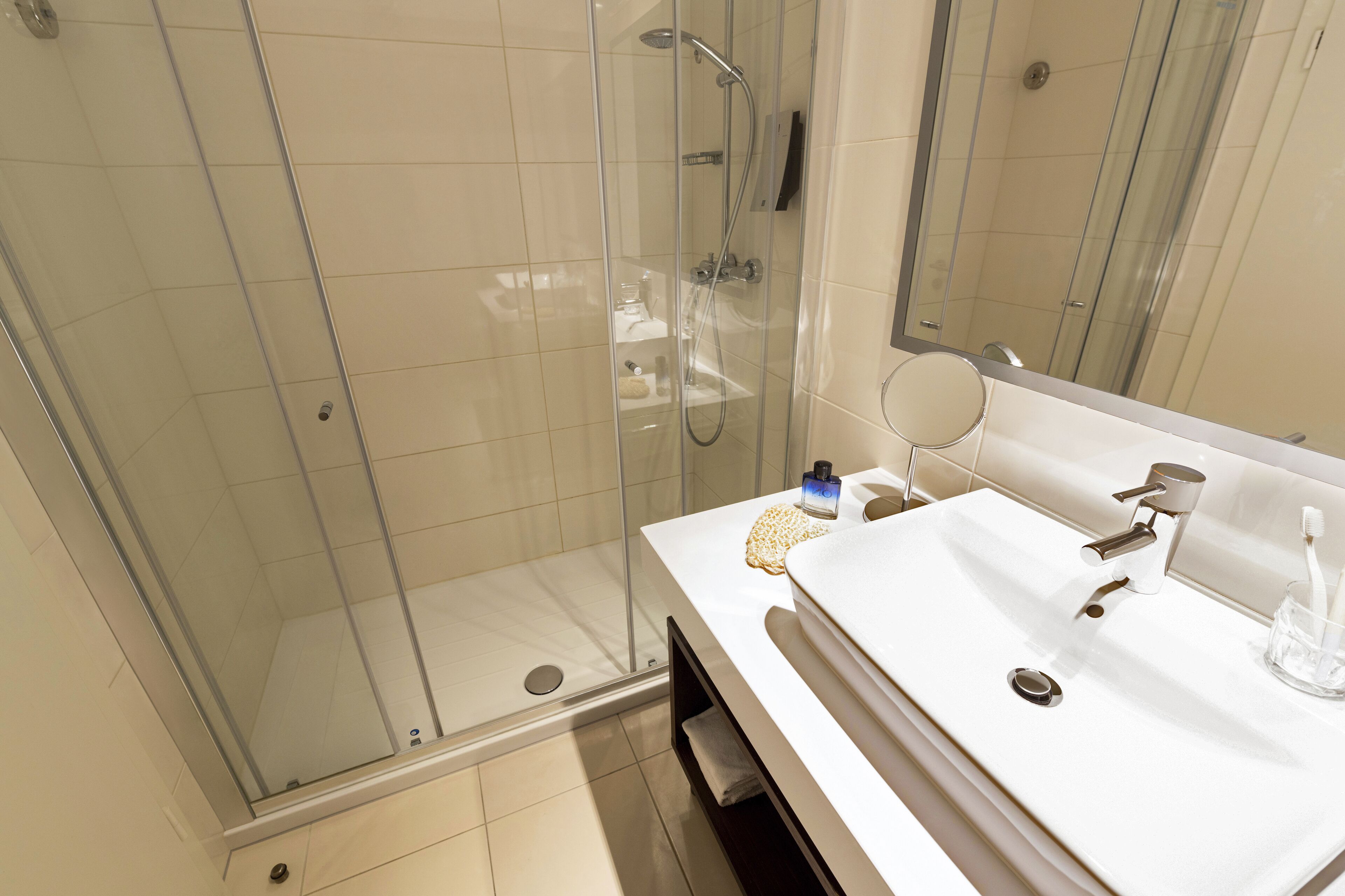 A modern bathroom with a glass-enclosed shower, a white sink with a mirror, and a towel rack.