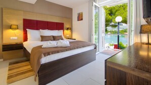 Habitación de hotel moderna con una cama grande, cabecera de madera, mesita de noche con lámpara y vista al mar por la ventana.