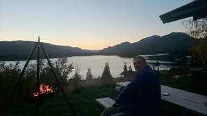 A person sitting on a wooden bench overlooking a lake with mountains in the background.