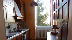 A kitchen with wooden cabinets, a gas stove, a window with a view of trees, and a patterned floor.