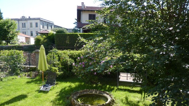 A well-maintained garden with a small pond, a bench, and an umbrella.