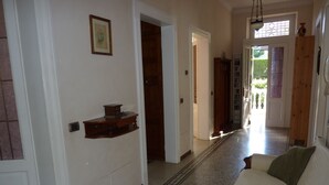 A hallway with a patterned floor, a wooden shelf with a small box, and a white sofa with a green pillow.