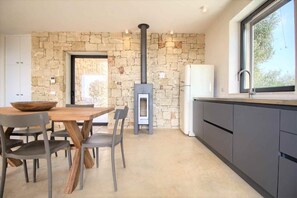Eine moderne Küche mit Steinwand, Kaminofen, grauen Schränken und einem großen Fenster.