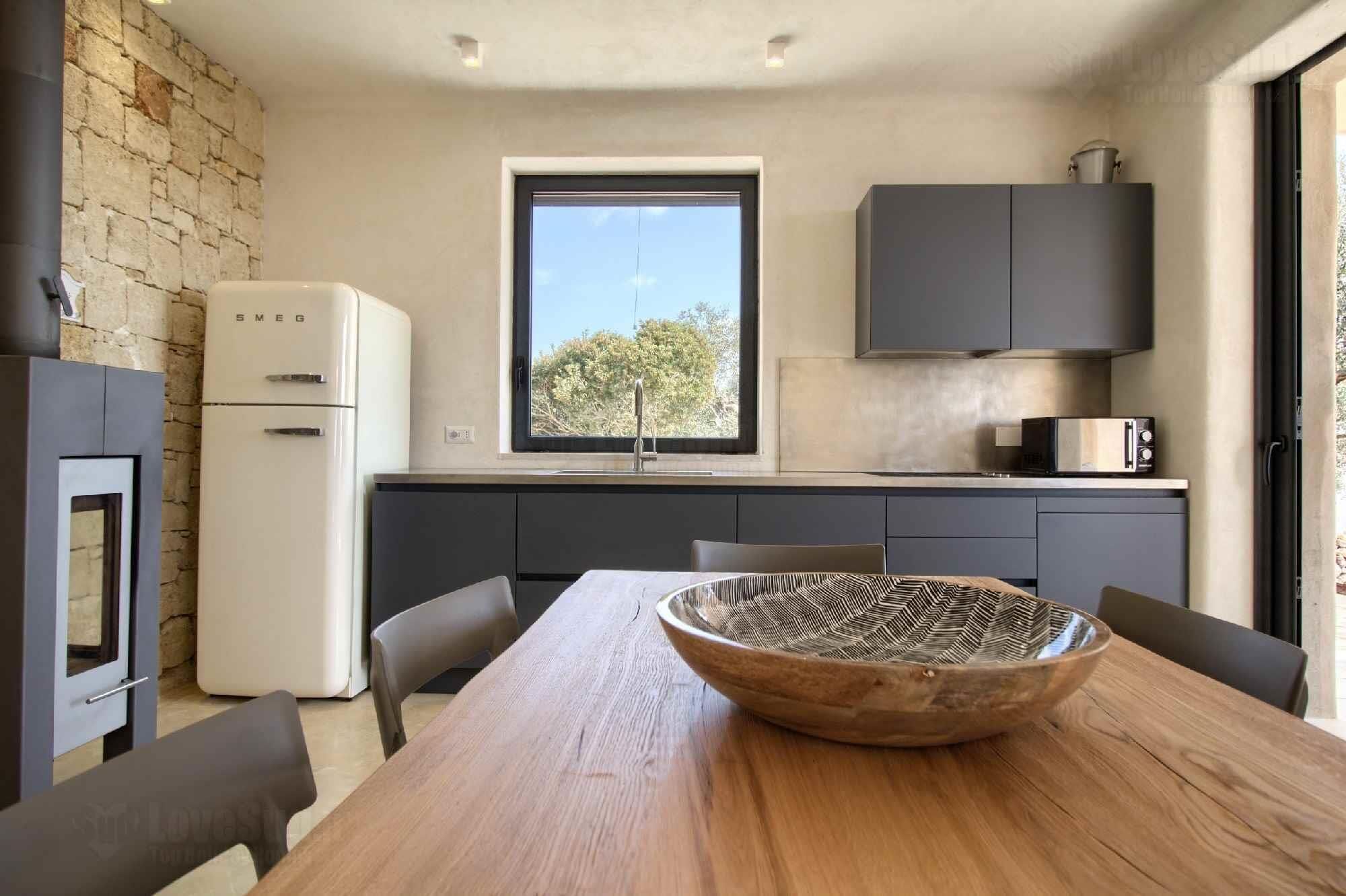 Una cocina moderna con un ventanal grande, estufa integrada y una mesa de madera con un cuenco tejido.