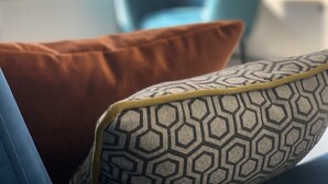 Primer plano de un cojín estampado sobre un sofá, con una silla azul al fondo.