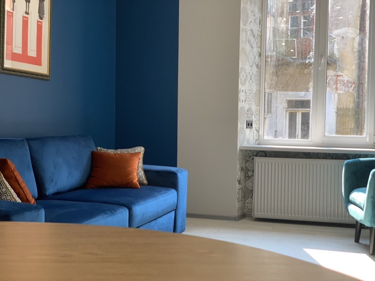 A room with a blue sofa, a wooden table, and a window with a view of buildings.