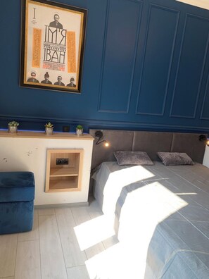 A bedroom with a bed, a small desk, and a wall-mounted shelf with plants.