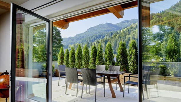 Een balkon met een tafel en stoelen, een wereldbol en uitzicht op een bebost gebergte.