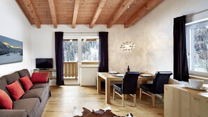 Een moderne woonkamer met een houten plafond, een bank met rode kussens, een eettafel met stoelen en een uitzicht op een besneeerd landschap door het raam.