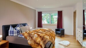 Een slaapkamer met een bed, nachtkastje, kaptafel en een raam met gordijnen.