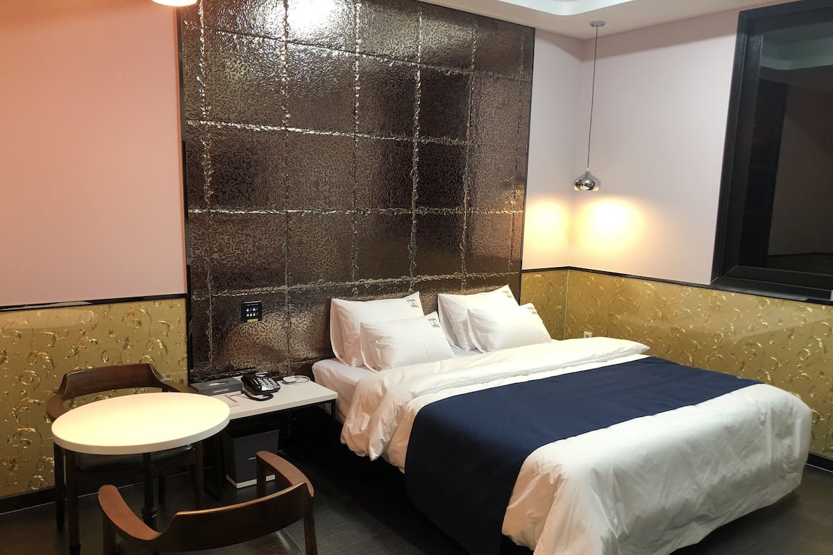 A hotel room with a bed, bedside table, chair, and a wall with a textured pattern.