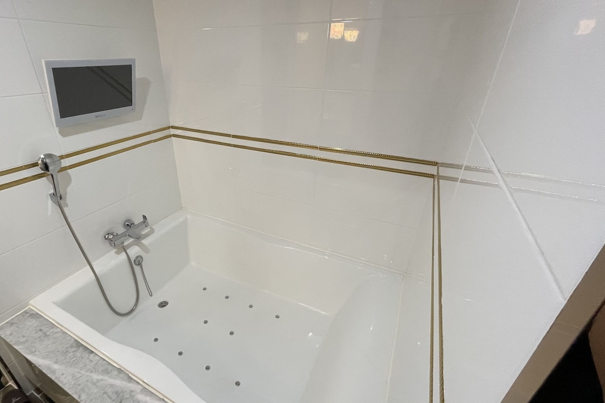 A modern bathroom with a glass-enclosed shower, white tiles, and gold trim.