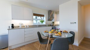 A modern kitchen with white cabinets, a glass dining table, and a compact refrigerator. - Sea Scapes – Sleeps 2/4 – Sea Views – Dog-Friendly - On-Site Parking (St Ives)