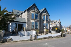 Une maison en pierre à deux étages, dotée d’une baie vitrée, d’un garage et d’une allée bordée de clôtures.
