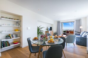 A modern living room with a glass dining table, a sofa, and a TV. - Sea Scapes – Sleeps 2/4 – Sea Views – Dog-Friendly - On-Site Parking (St Ives)