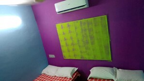 A room with two beds, purple walls, a ceiling fan, and an air conditioner. - serenity beach house (puducherry)