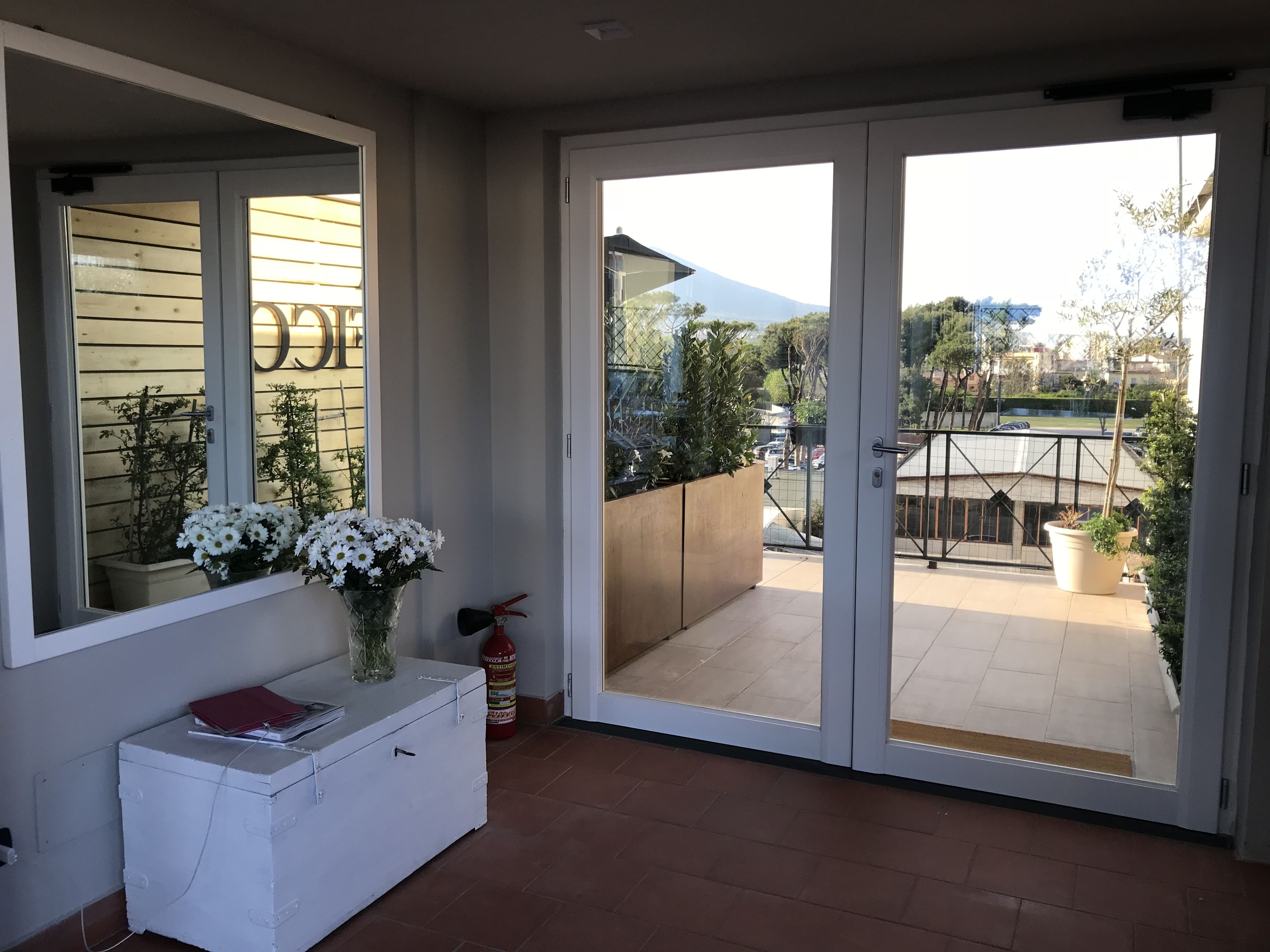 A balcony with a sliding glass door, a white storage unit, and a vase with white flowers.