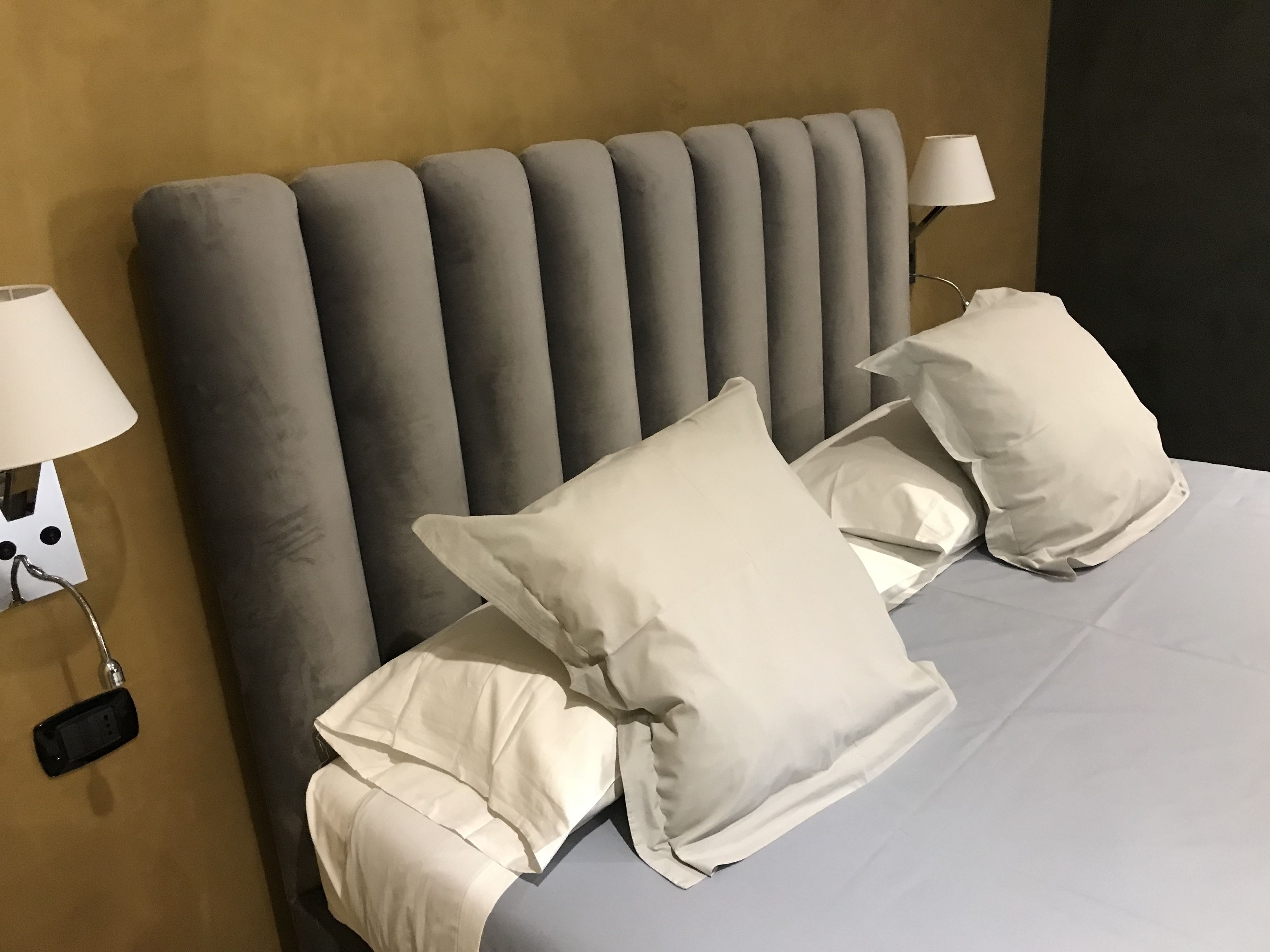 Una cama bien hecha con un cabecero tapizado en gris, almohadas blancas y una colcha gris.
