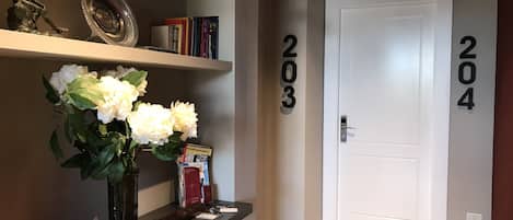 Un pasillo con un tablero de ajedrez, un jarrón de flores y libros en una estantería. Se ven los números 203 y 204 en la pared.