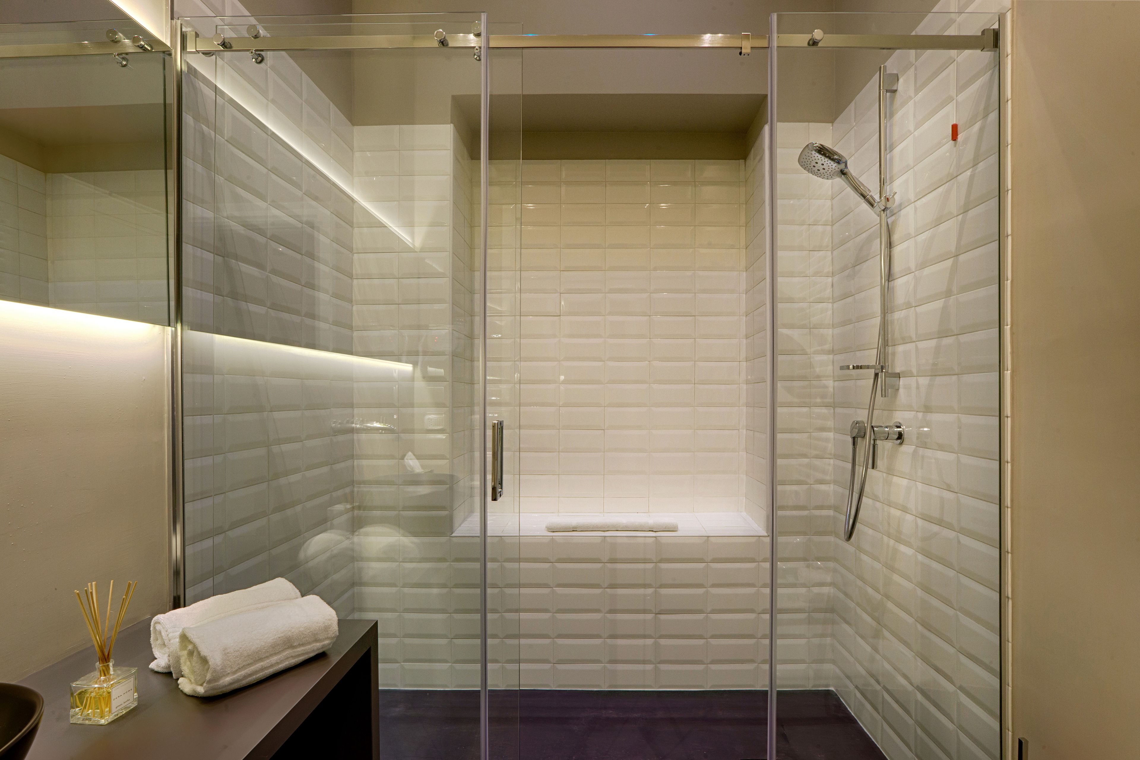 A modern bathroom with a glass-enclosed shower, white tiled walls, and a bench.