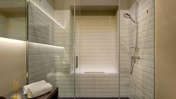 A modern bathroom with a glass-enclosed shower, white tiled walls, and a bench.