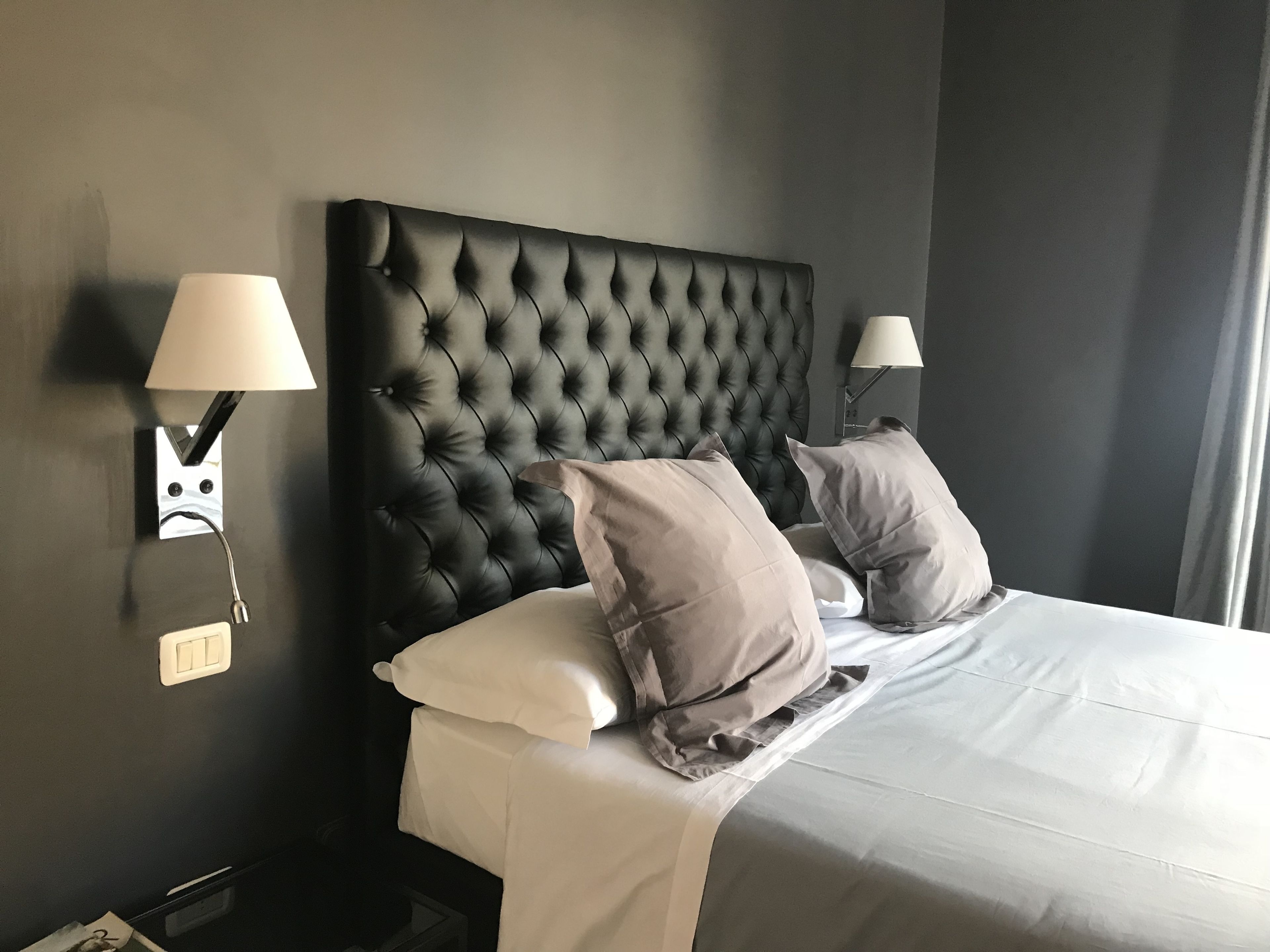 A hotel room with a tufted headboard, two bedside lamps, a bed with white linens, and a nightstand with a lamp.