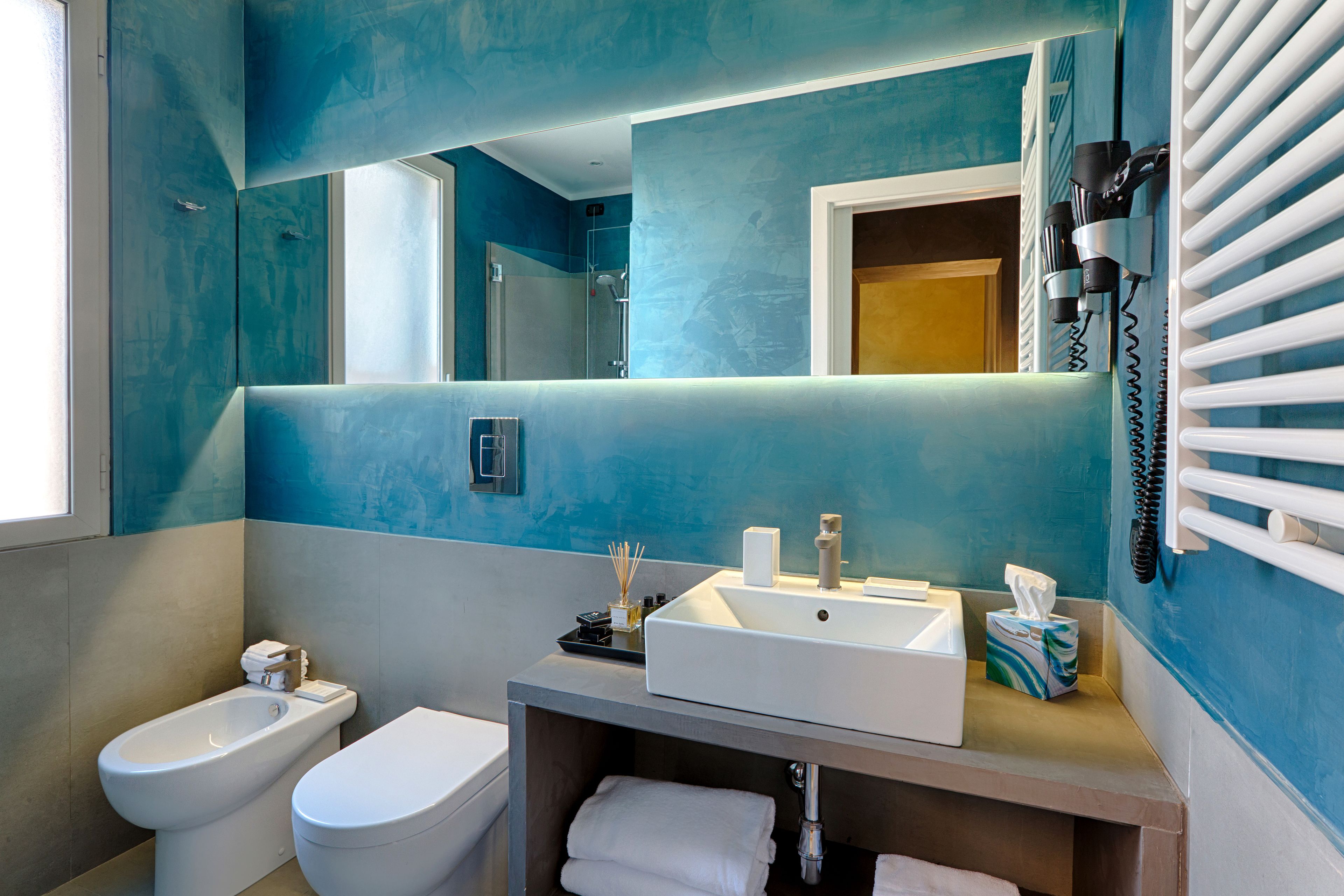A modern bathroom with a large mirror, a sink, a bidet, and a towel rack.
