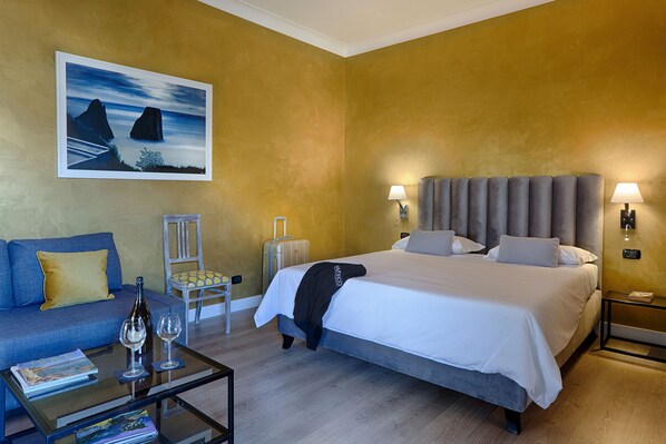 A hotel room with a bed, a sofa, a glass coffee table, and a painting on the wall. - Casa Pacifico (Pompei)