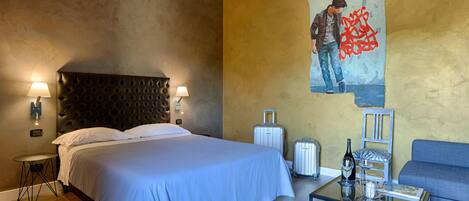 Una habitación de hotel con una cama grande, una mesa de centro de vidrio, un sofá y un cuadro en la pared.