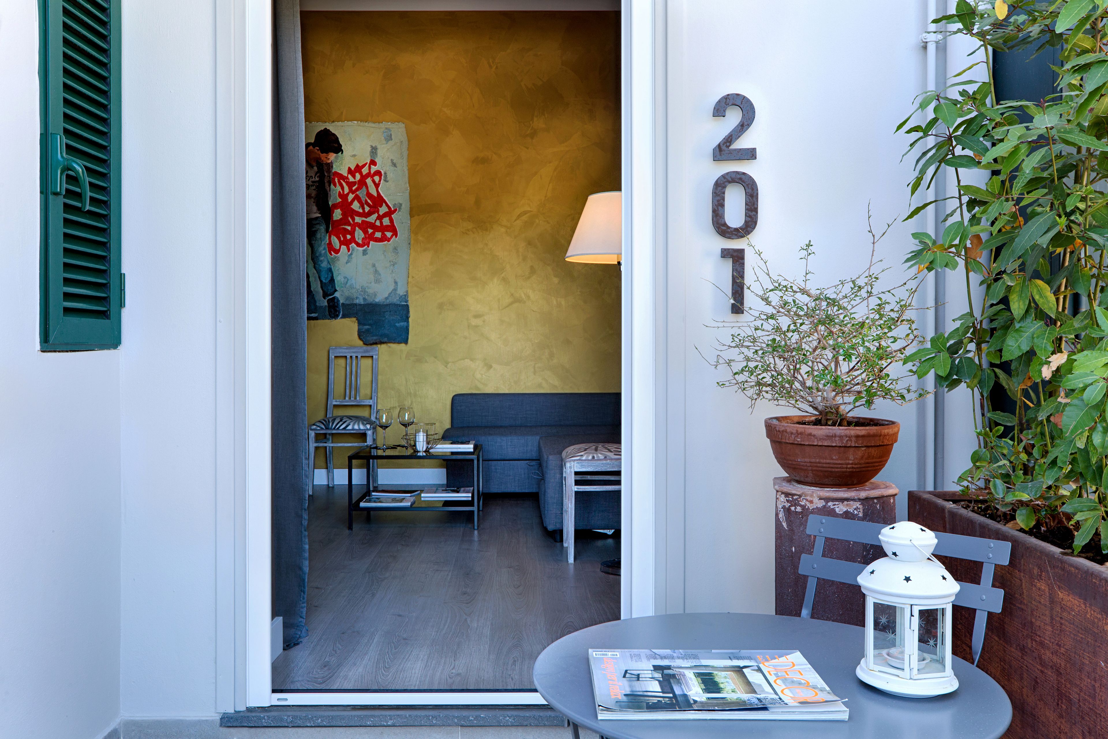 A hotel entrance with a number '201' on the wall, a small table with a magazine, a potted plant, and a lamp.
