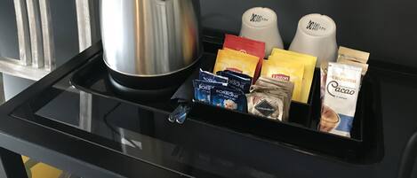 A tray with a coffee maker, Lipton tea bags, and instant coffee packets on a black table.