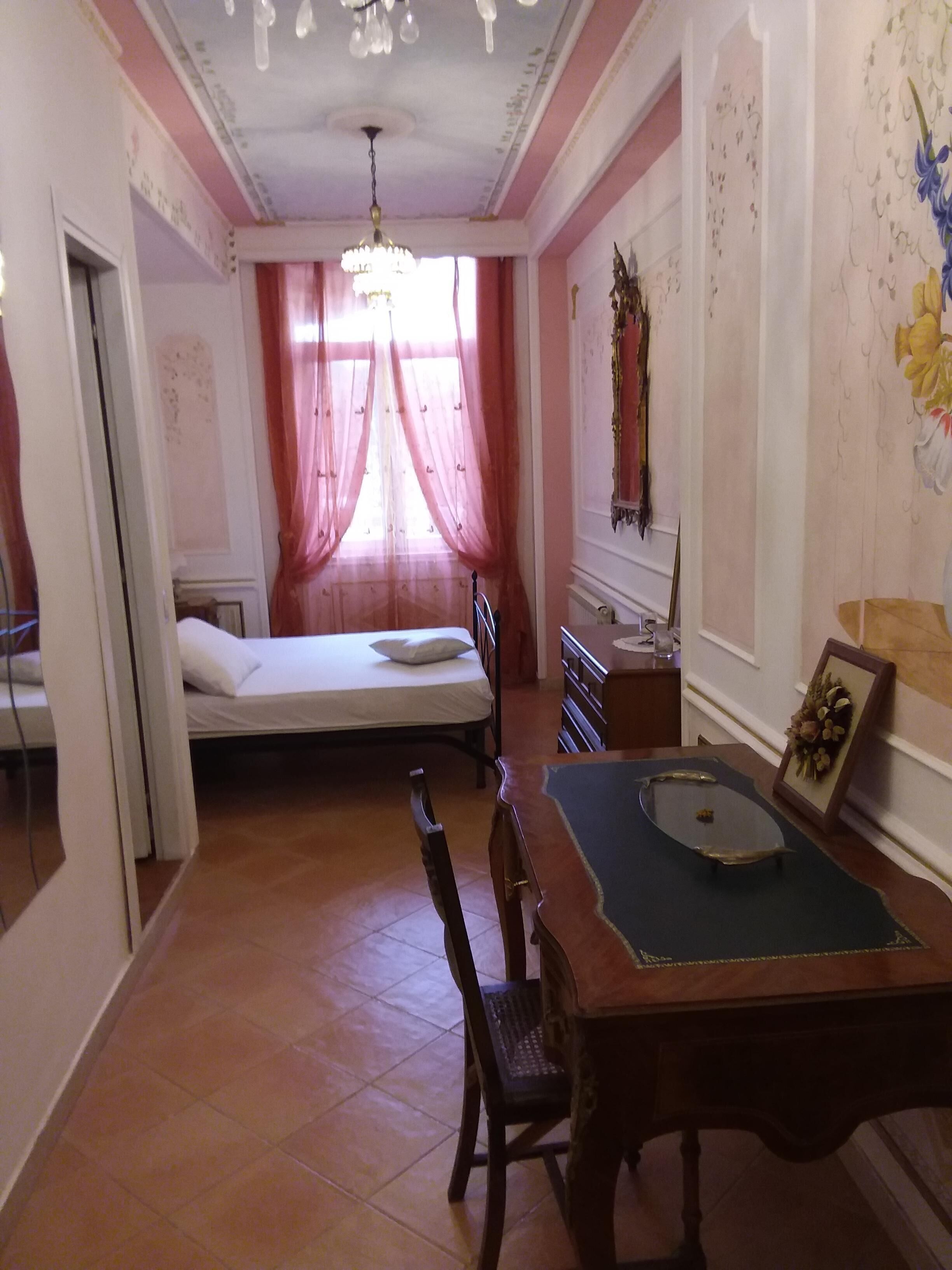 A room with a bed, a desk, a chair, and a chandelier.