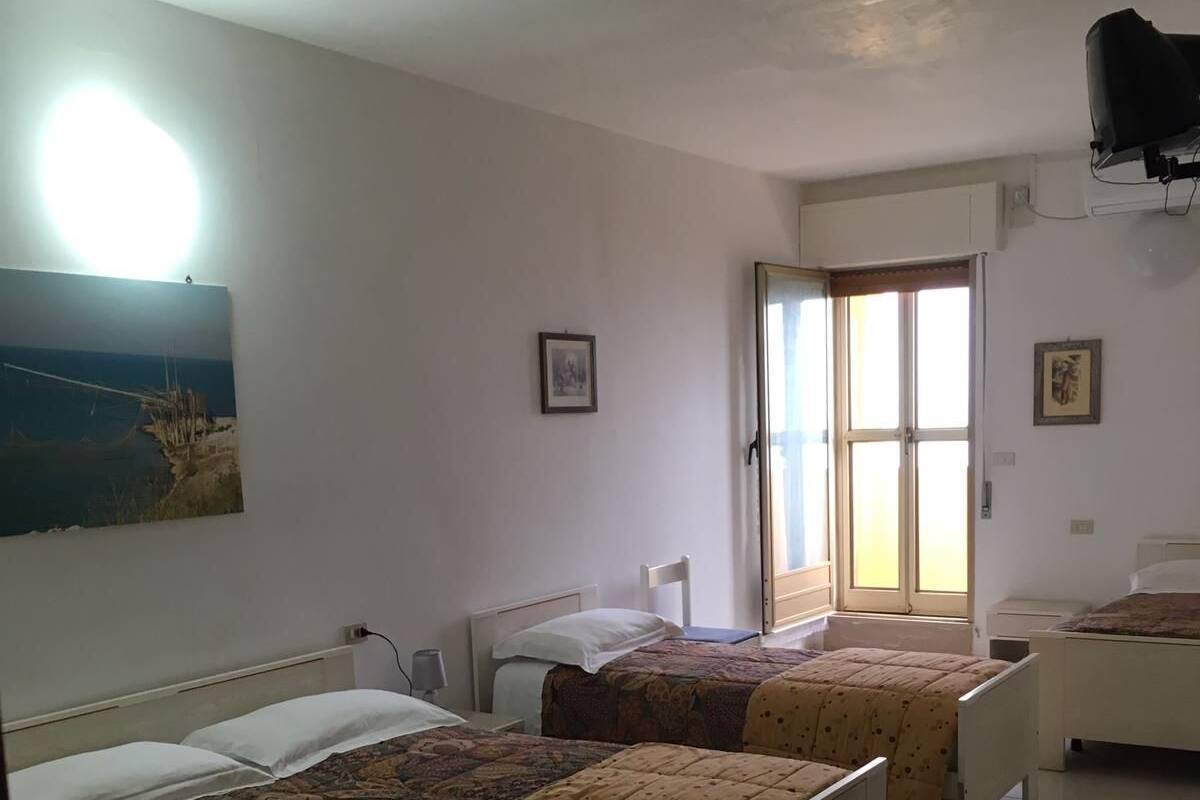 Une chambre avec deux lits, une grande fenêtre et un ventilateur de plafond.