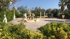 Een klassieke fontein met leeuwen, omringd door weelderige begroeiing en palmbomen.