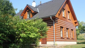A log cabin with a steeply pitched roof, a chimney, and a large window.